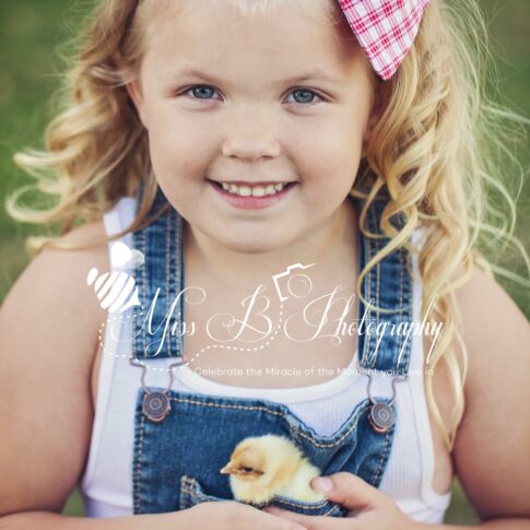 little girl in overalls darm shoot with baby chicken