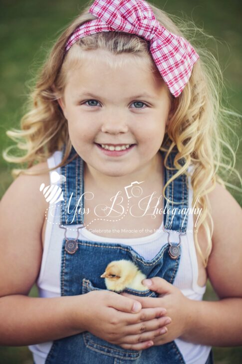 little girl in overalls darm shoot with baby chicken